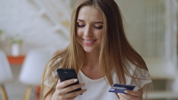 Beautiful young woman have online banking and shopping using smartphone and debit card at home