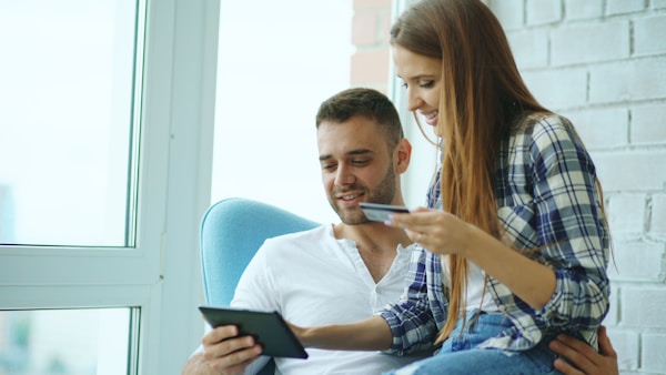 Young cheerful couple using digital tablet computer for online shopping sitting on balcony in modern loft apartment
