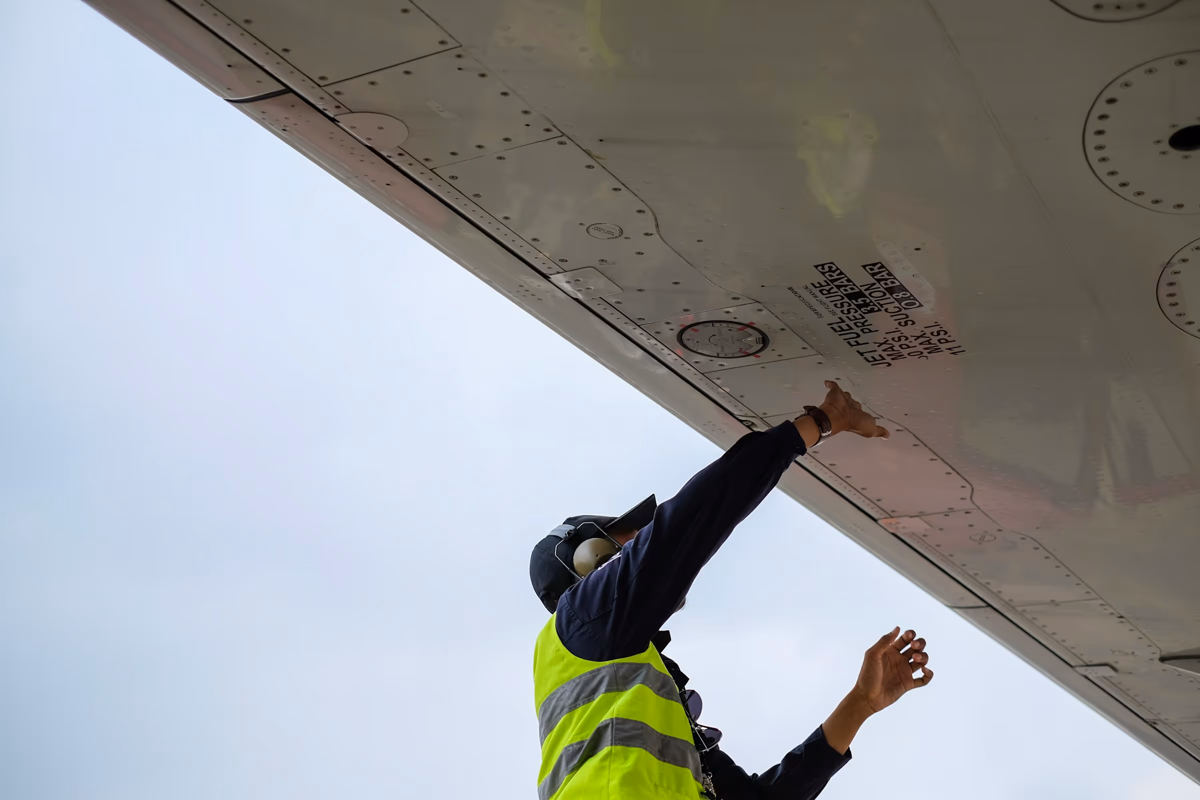 Technician examining an aircraft’s exterior from below the wing.