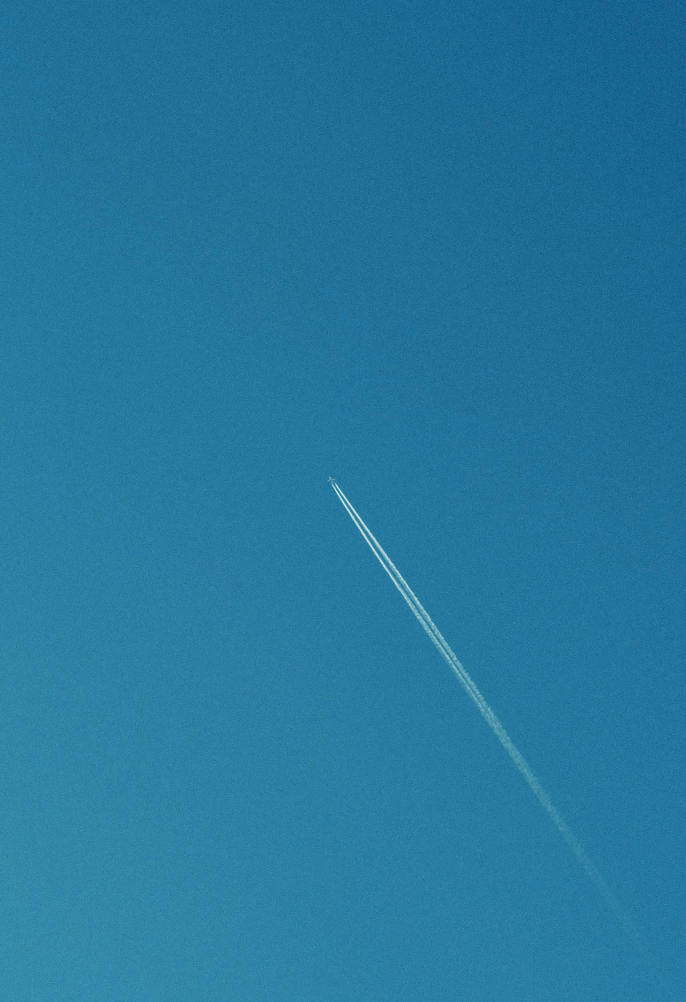 Airplane flying at high altitude, leaving a contrail in a clear sky.