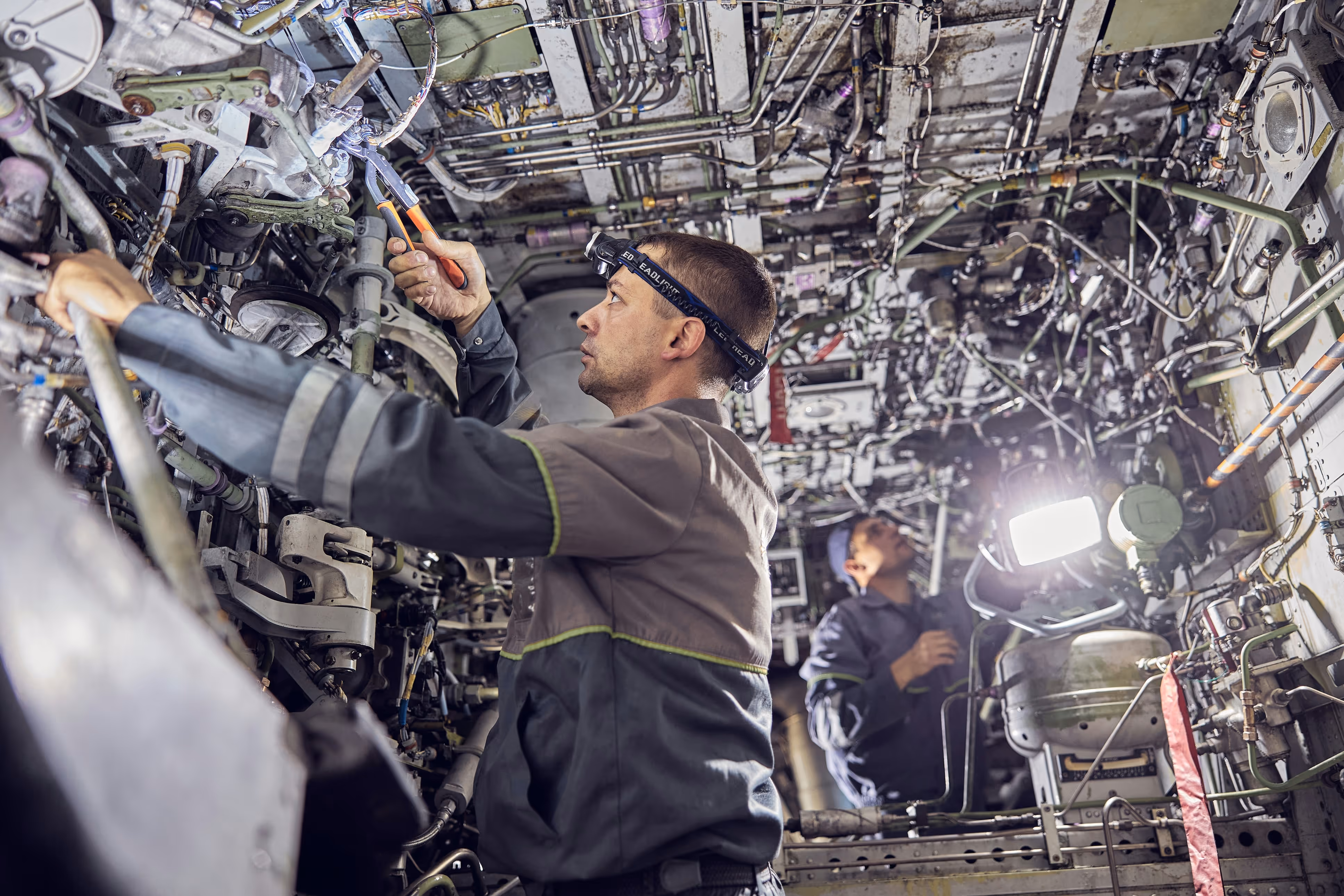 Aircraft mechanic performing inspection inside airplane’s mechanical bay.