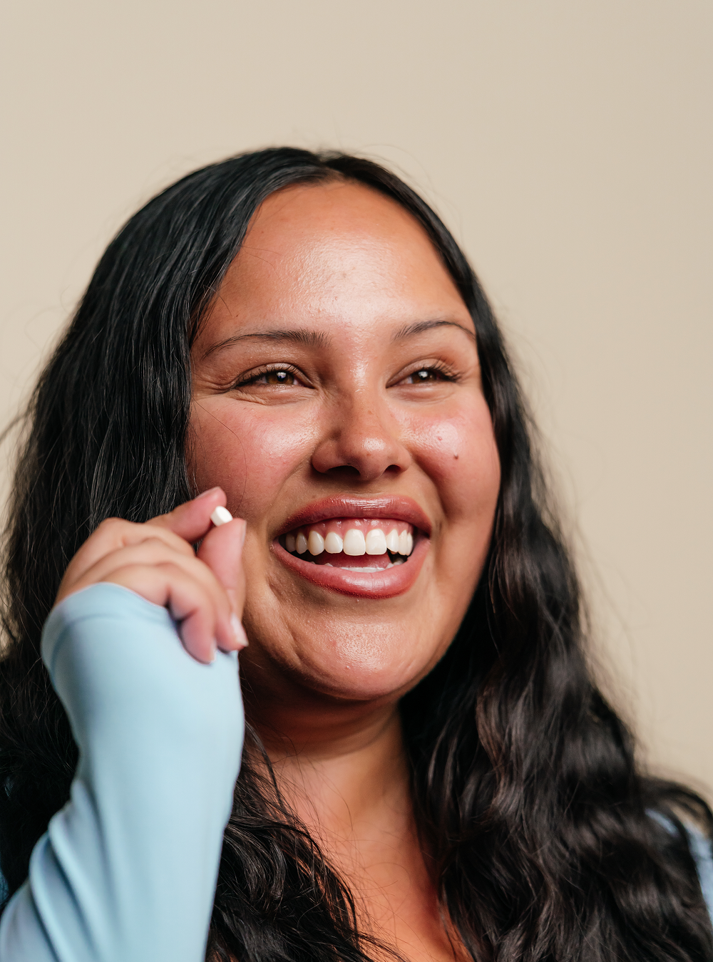 Woman with long hair holding a small pill smiling.