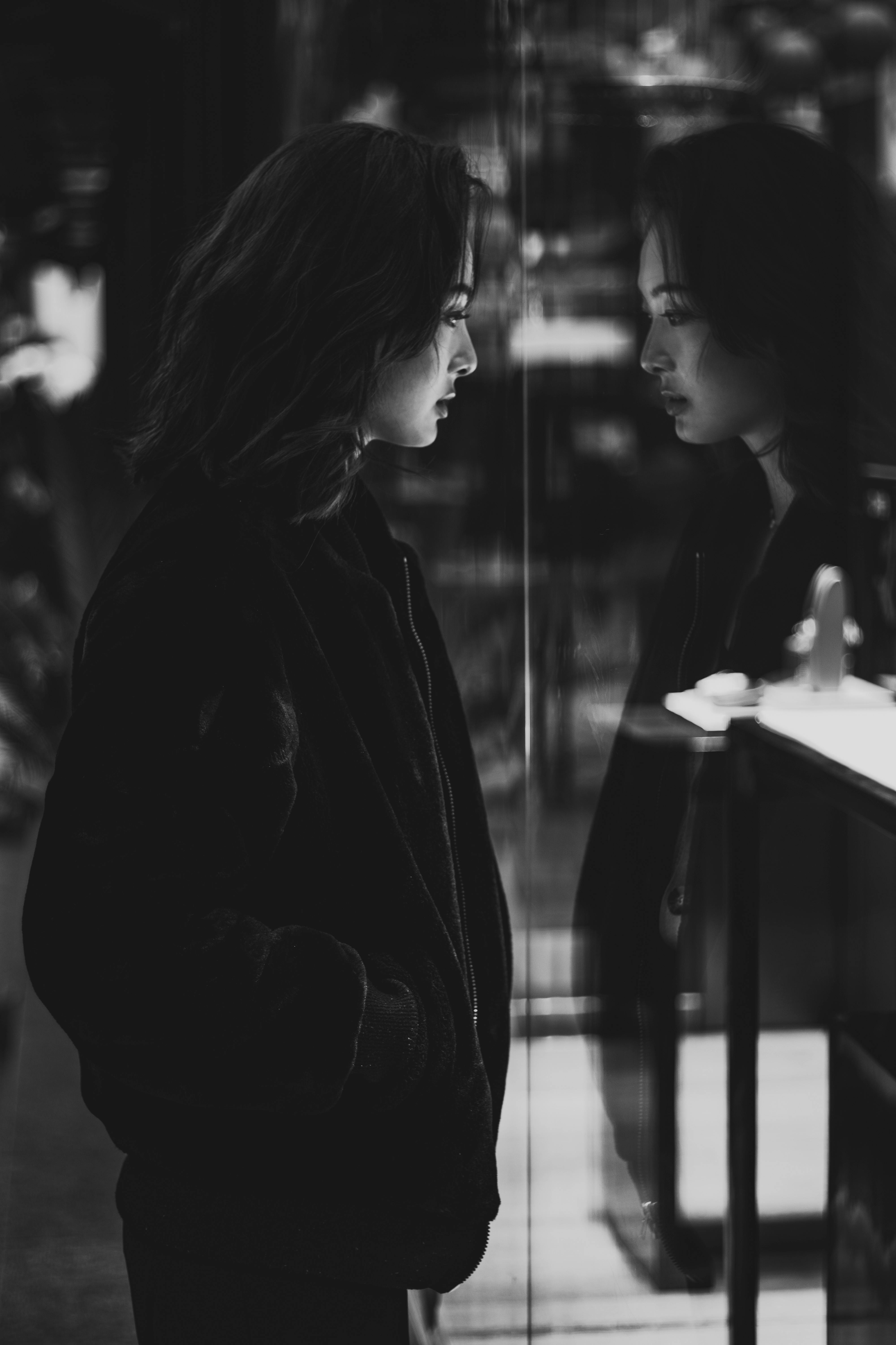 Asian Woman in Black Jacket Standing Beside Mirror