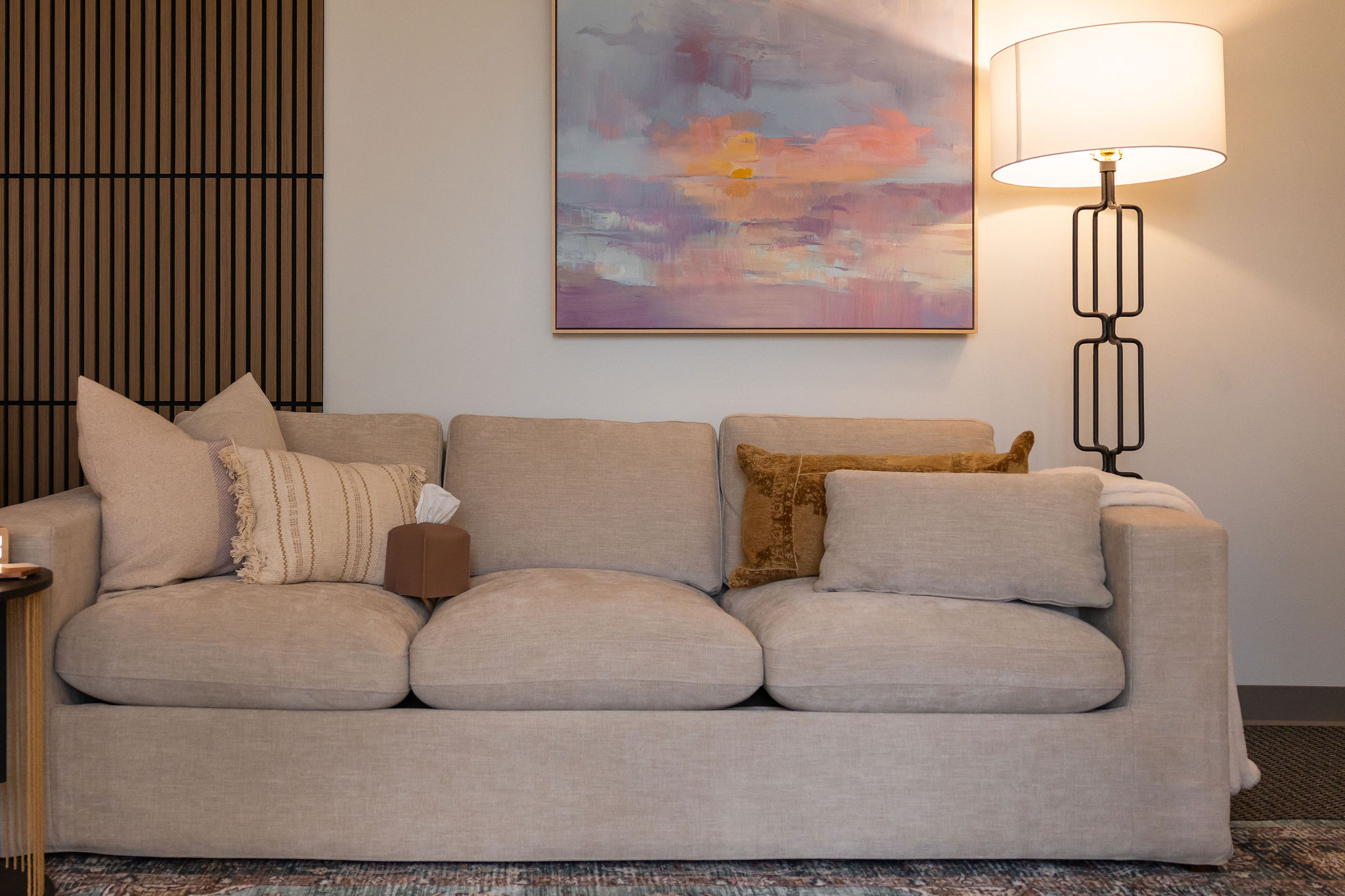Clear Mind's therapy office featuring a beige sofa with beige decorative pillows, a black floor lamp, and a pastel abstract art