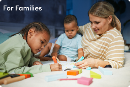 A woman and two children are sitting on a bed, working on a coloring book. - Hopscotch Images