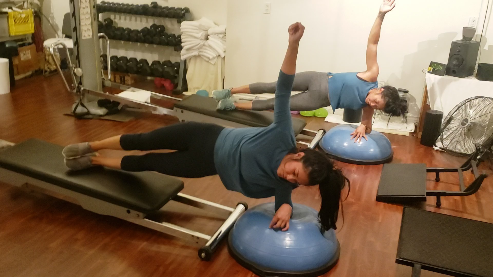 Two women performing side plank balance exercises on BOSU balls and Total Gym equipment at Tsquared Personal Training in Downtown Vancouver, guided by personal trainer Troy Tyrell.