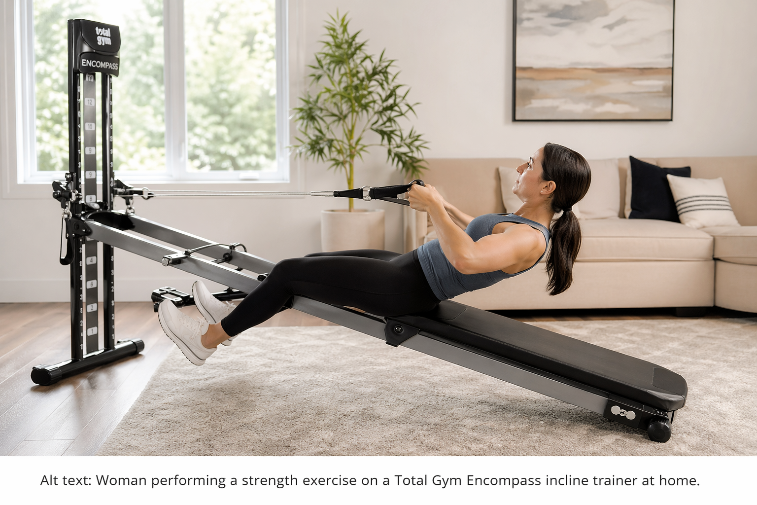 Woman performing a low-impact strength exercise on a Total Gym Encompass incline trainer in a bright home gym.