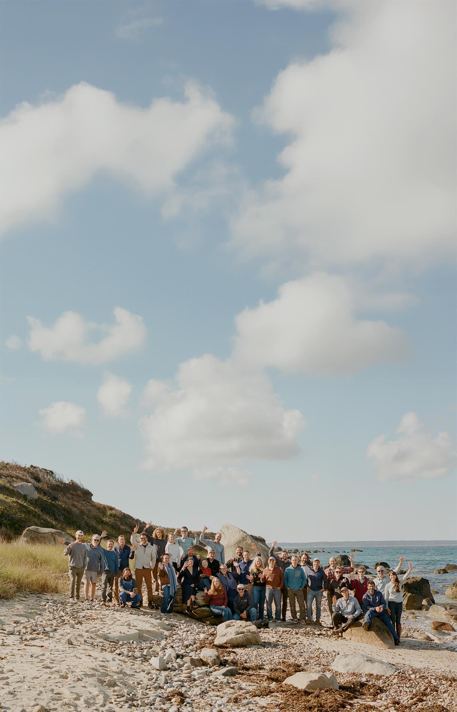A large group of people standing on the beach waving at the camera.