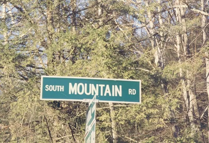 Green street sign reading 'South Mountain Rd' mounted on a metal post, surrounded by bare winter trees