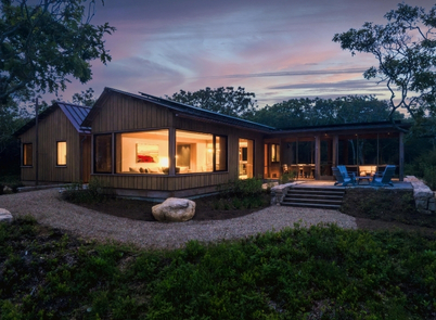 Lovely new house nestled in the landscape, lit from within at dusk