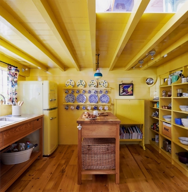 Warm yellow vintage cottage kitchen with blue plates displayed on wall, open shelving and an old fashioned refrigerator.
