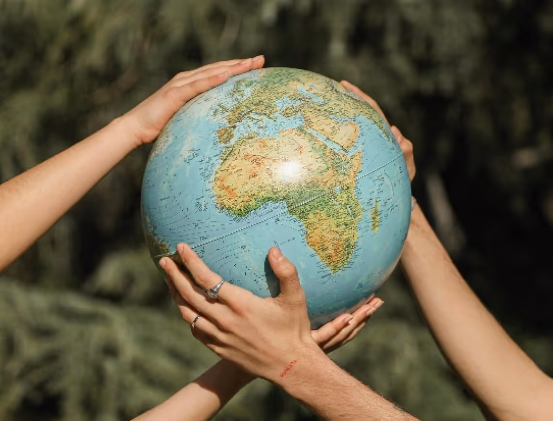 Four hands holding a globe, with a focus on Africa, against a blurred green background. The image conveys a sense of unity and global awareness.