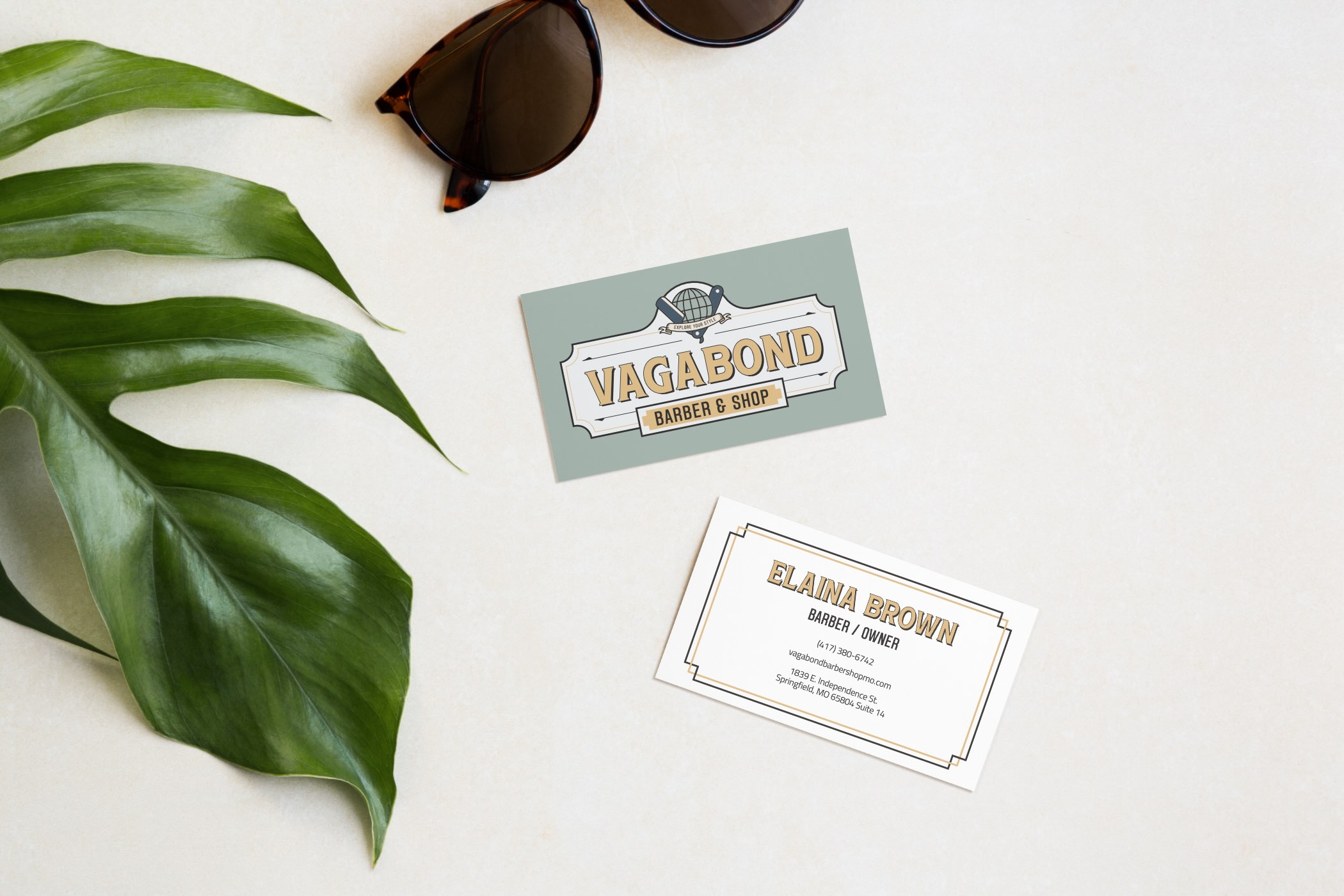 Business card mockup for Vagabond barbers. Vintage looking logo with a straight razor in the shape of a "v" surrounding a globe. 