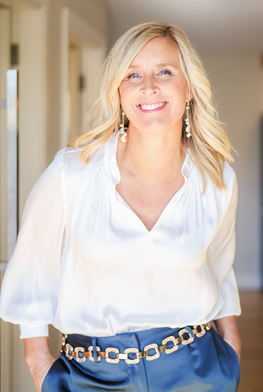 Belle smiling in white blouse and blue pants with a gold chain belt