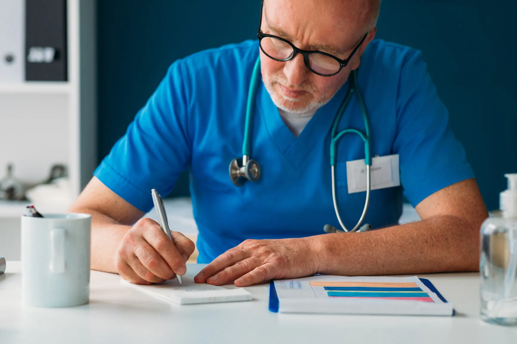 A clinician in scrubs writing up notes at a desk after a consultation