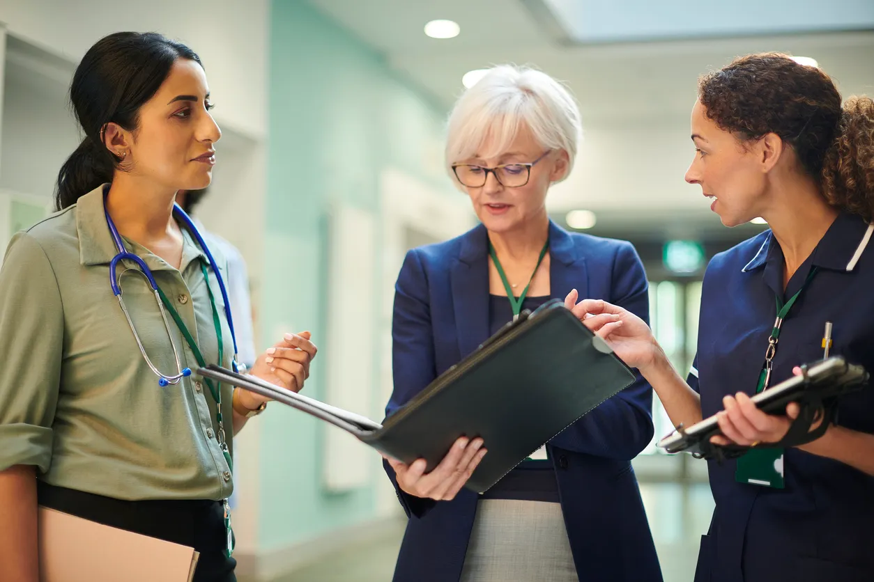 Three clinicians reviewing patient notes together in a hospital corridor