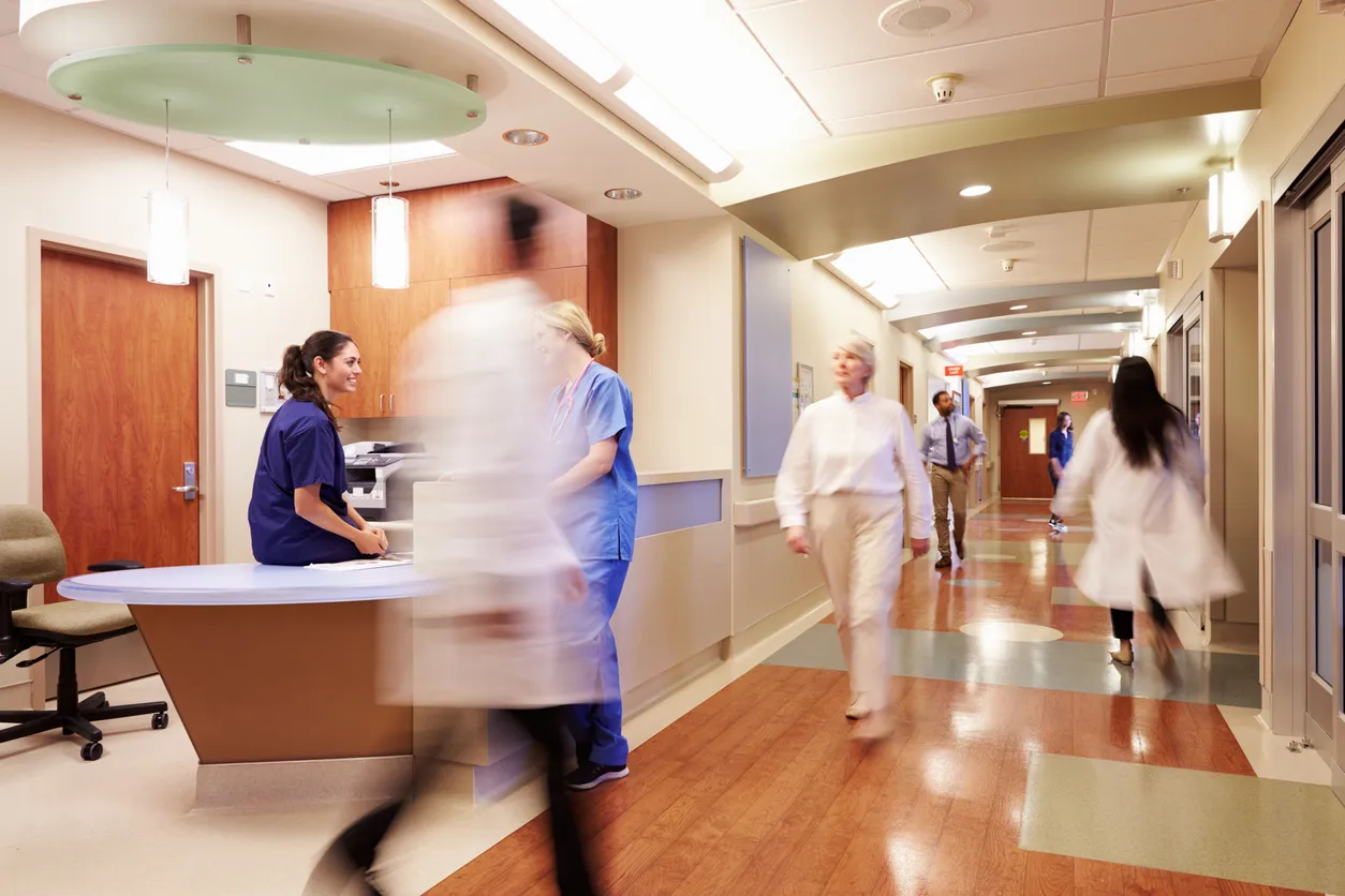 Staff and patients moving through a busy hospital corridor and nurses station