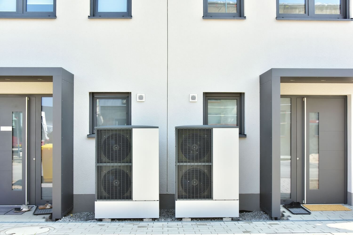 Hybridheizung Gas & Wärmepumpe: Zwei Wärmepumpen stehen vor modernen Wohnhäusern.