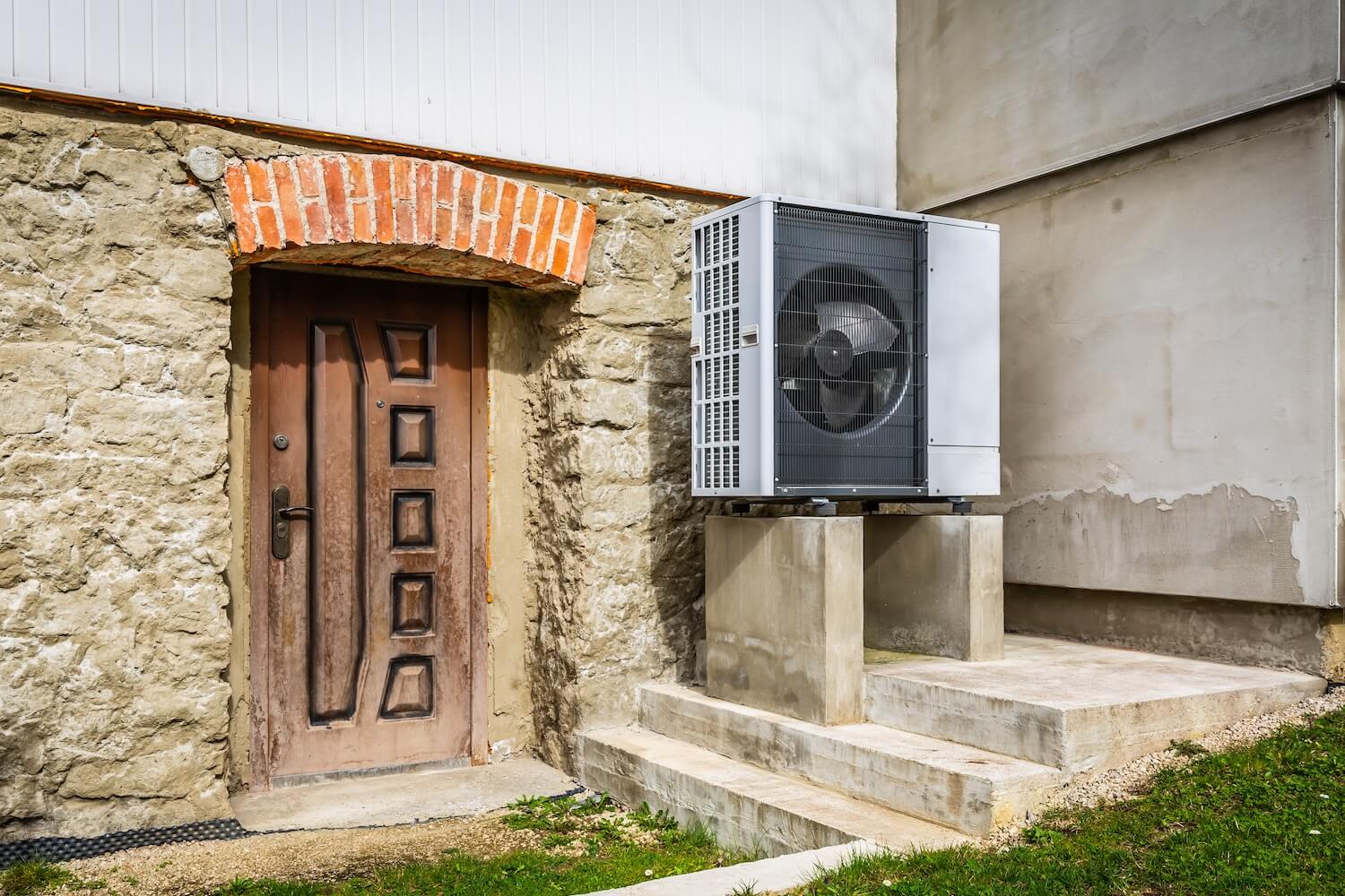 Wärmepumpe auf Betonfundament neben alter Kellertür aus Holz und Stein – Symbolbild für Altbausanierung.