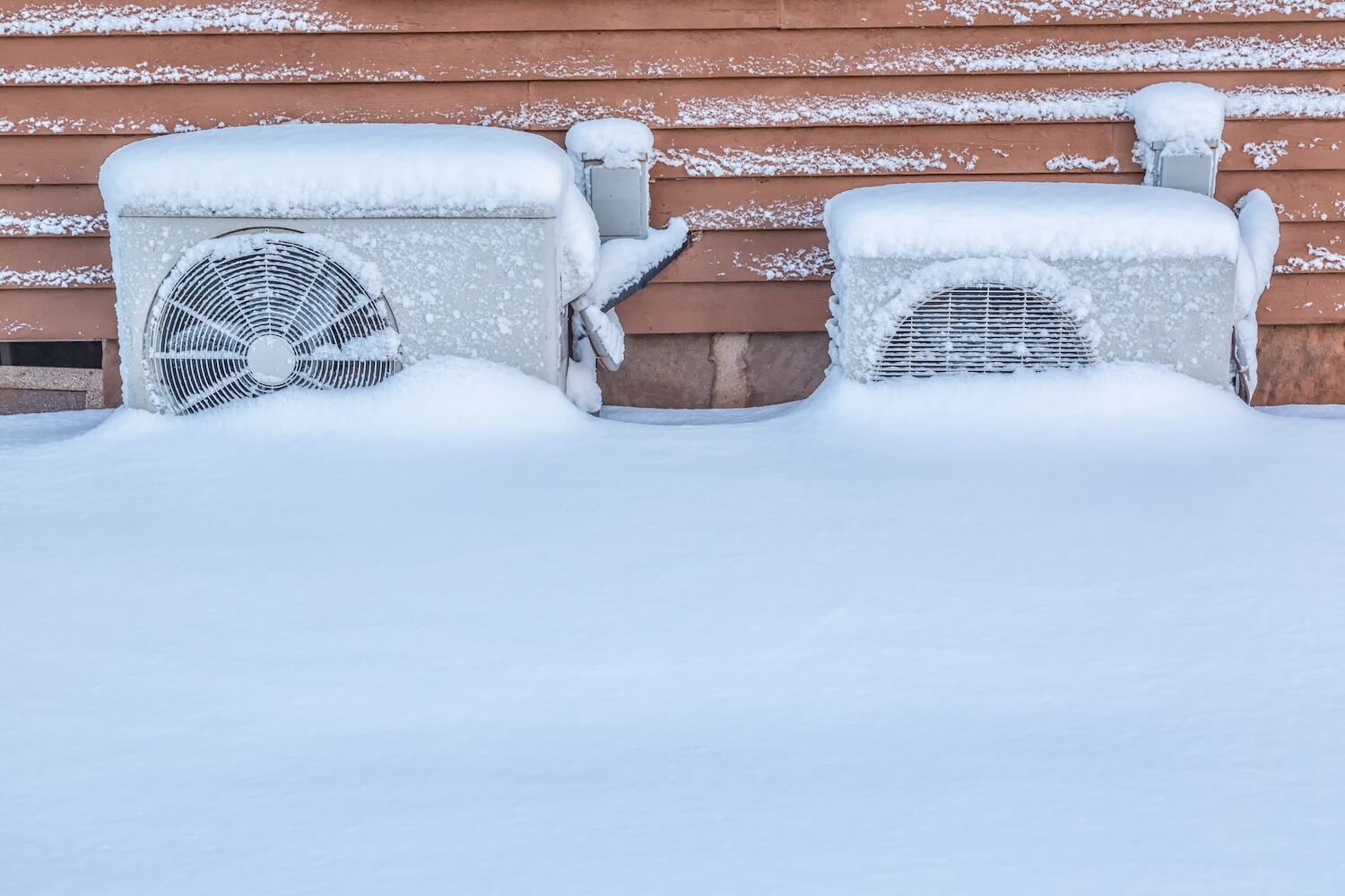 Zwei Wärmepumpen im Winter, vollständig von Schnee bedeckt – gegen Folgeschäden können Sie Ihre Wärmepumpe versichern.