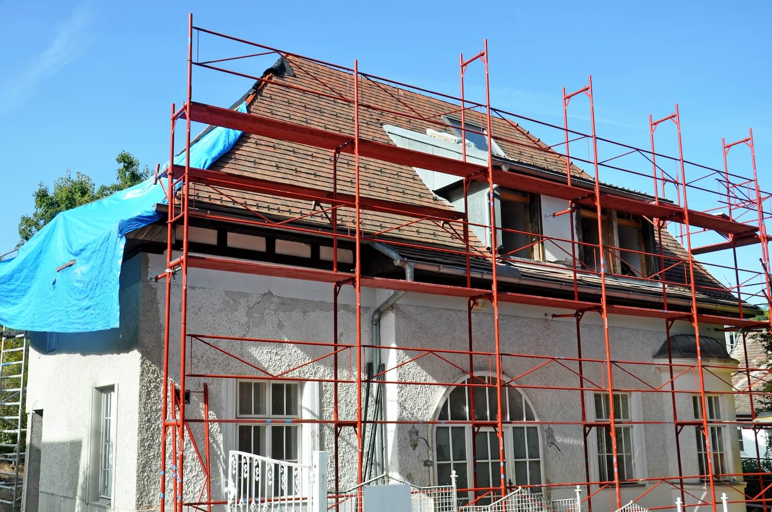 Wohnhaus mit rotem Baugerüst und blauer Plane bei Dachsanierung – typisches Bild für energetische Modernisierung und Dämmung.