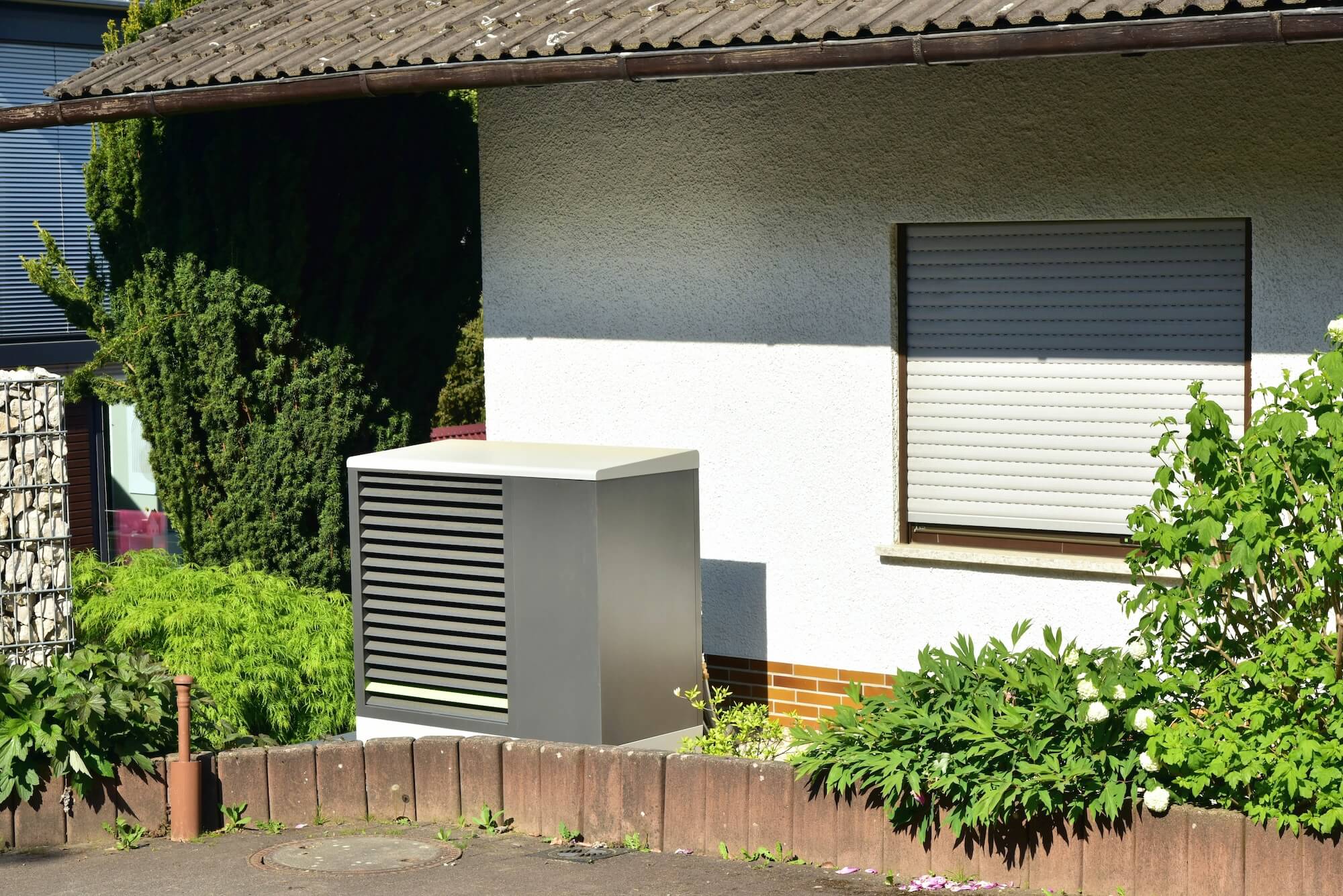 Eine Wärmepumpe mit Schallschutzhaube steht auf einem Betonfundament vor einem Wohnhaus.