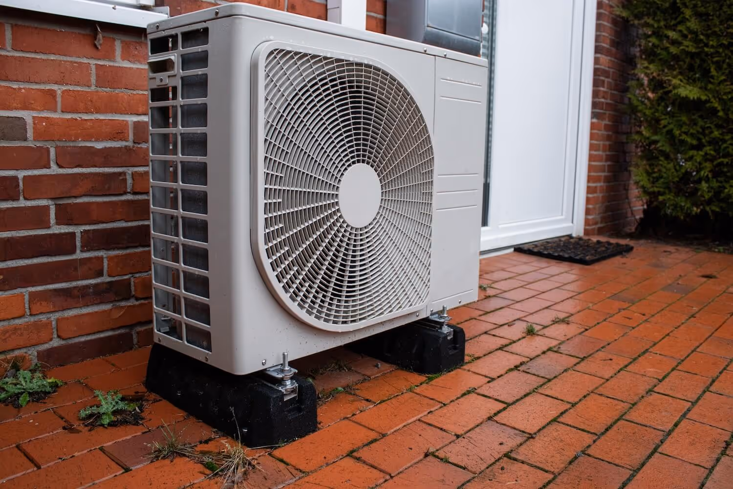 Moderne Heizung mit Luft-Wasser-Wärmepumpe-Außengerät an Ziegelwand montiert.