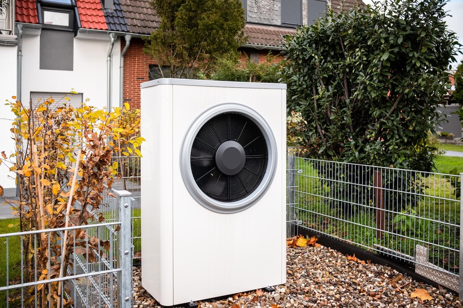 Eine weiße Wärmepumpe steht vor einem Wohnhaus.