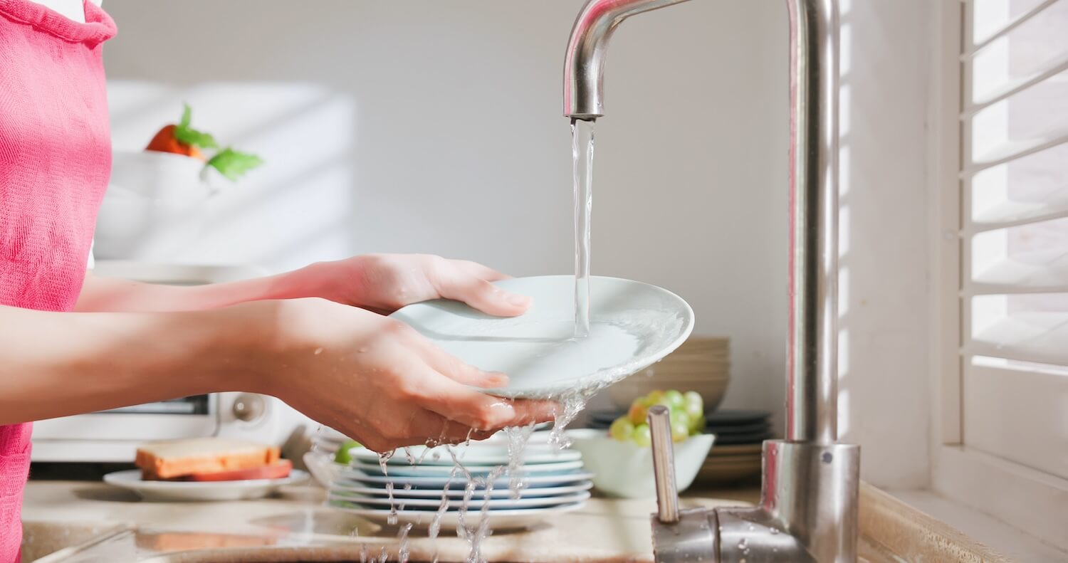 Eine Person spült ein Geschirr unter fließendem warmem Wasser, das durch eine Brauchwasser-Wärmepumpe erhitzt wurde.