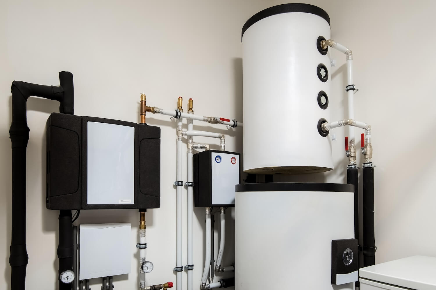 Ein modernes Brauchwasser-Wärmepumpensystem in einem Heizungsraum. Die Anlage besteht aus einem großen weißen Speicherbehälter und mehreren schwarzen und weißen Leitungen und Komponenten, die zur effizienten Erwärmung und Verteilung von Brauchwasser genutzt werden.