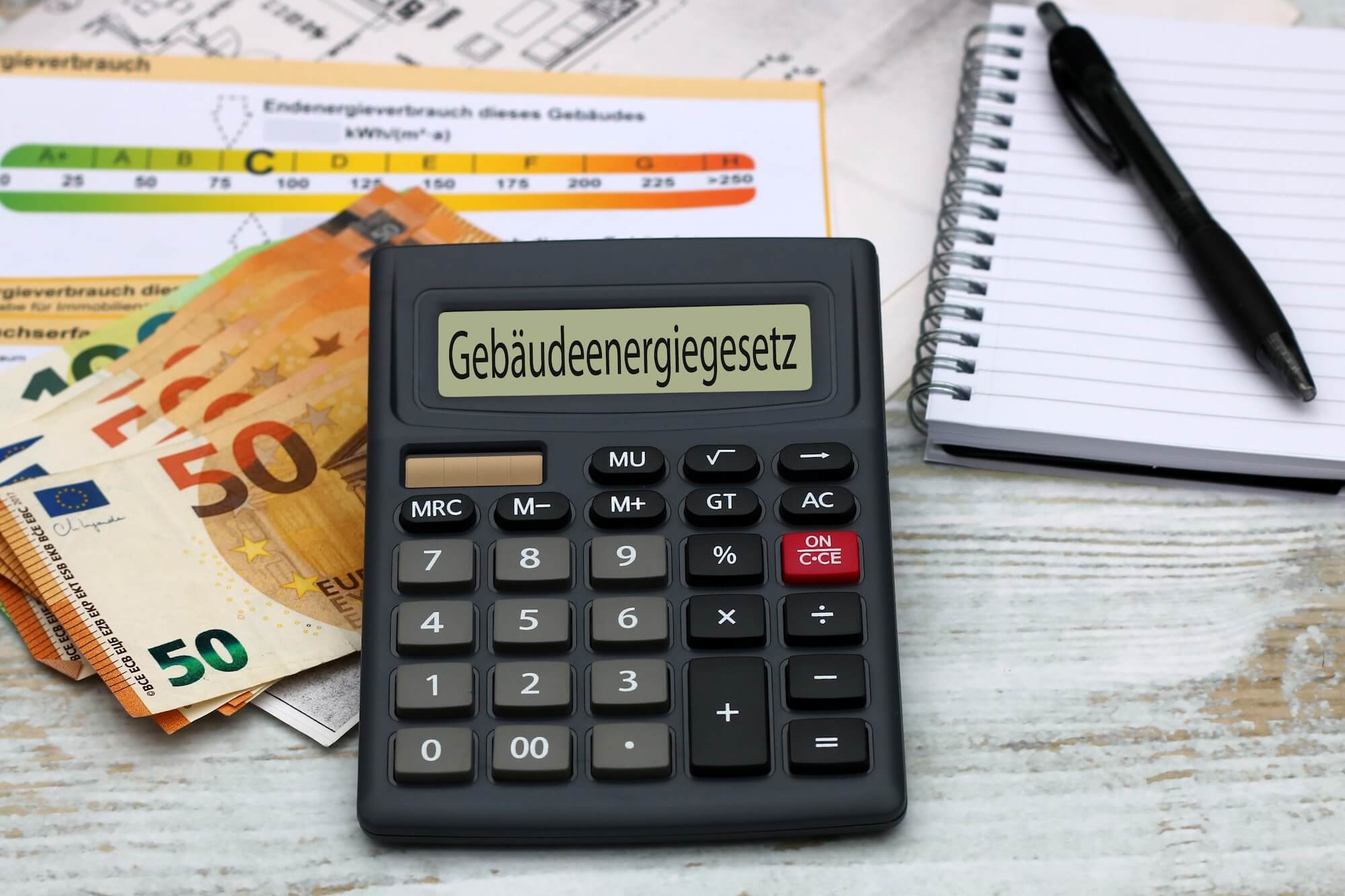 Ein Taschenrechner zeigt das Wort Gebäudeenergiegesetz an und liegt dabei auf einem Stapel Geldscheinen.