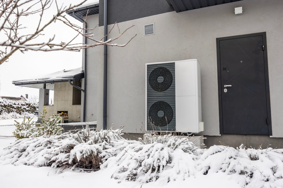 Hochtemperatur-Wärmepumpe im Winter bei Schnee vor einem modernen Einfamilienhaus