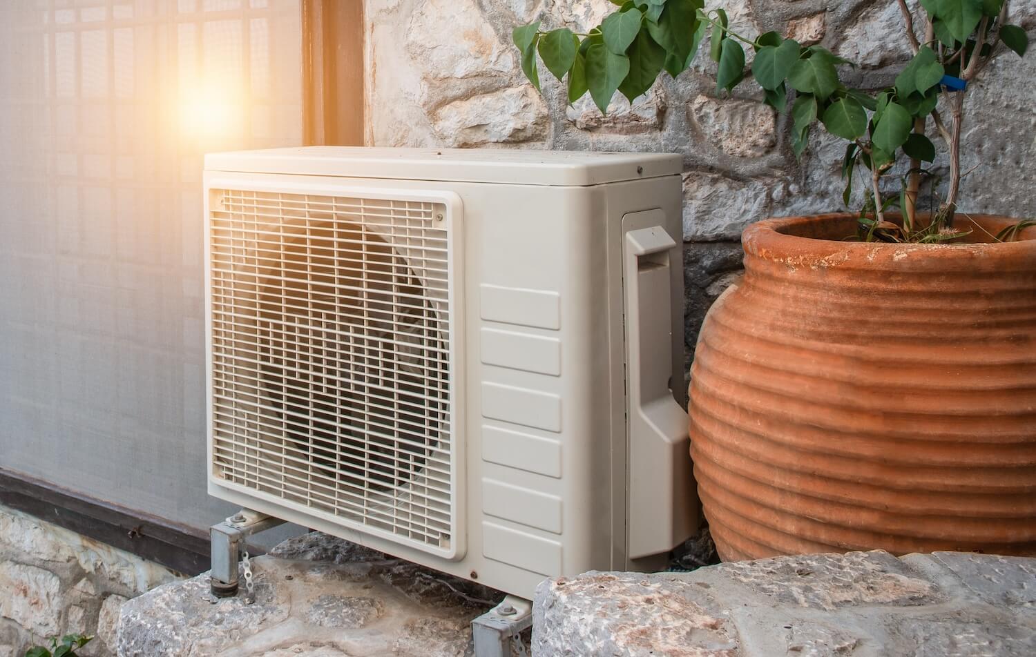 Kleine Wärmepumpe neben einer Steinmauer und Pflanzen