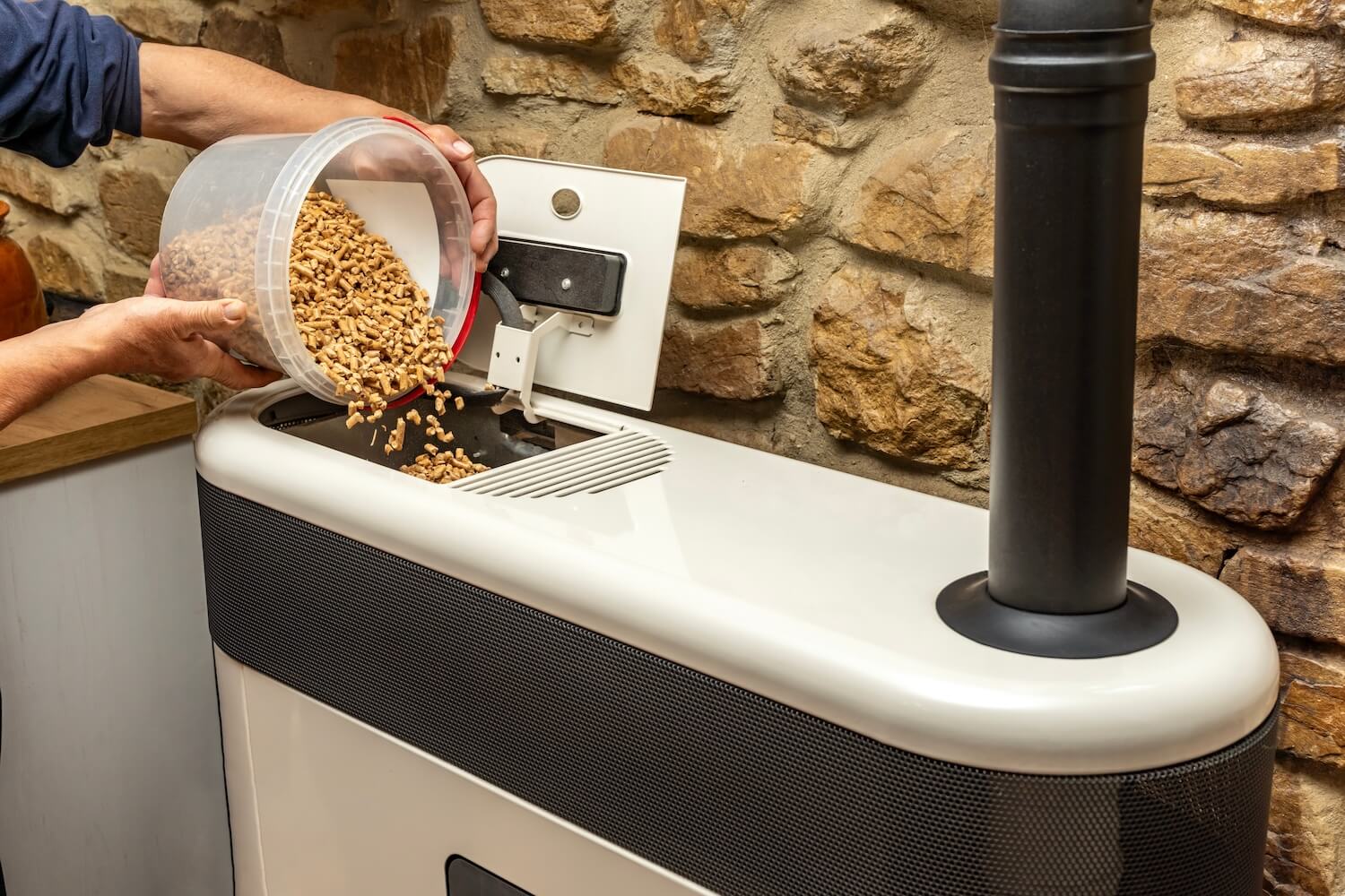 Nach dem Heizung erneuern sorgt eine moderne Pelletheizung für nachhaltige Wärme - hier bei der Befüllung mit Holzpellets vor rustikaler Natursteinwand.