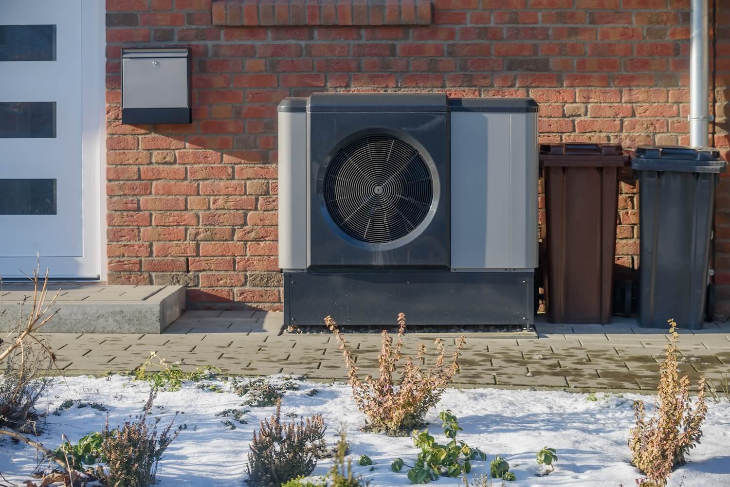 Moderne Luft-Wasser-Wärmepumpe als Alternative zum Kaminofen-Verbot: Außengerät an einer Ziegelwand im Winter.