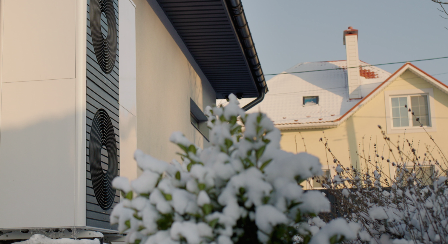 Wärmepumpe vor Hauswand in verschneitem Garten.