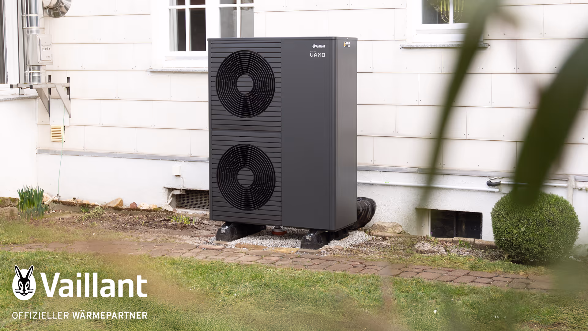 Von Vamo installierte Vaillant Wärmepumpe vor einer Hauswand. Unten links im Bild das Siegel "Offzieller Vaillant Wärmepartner"u