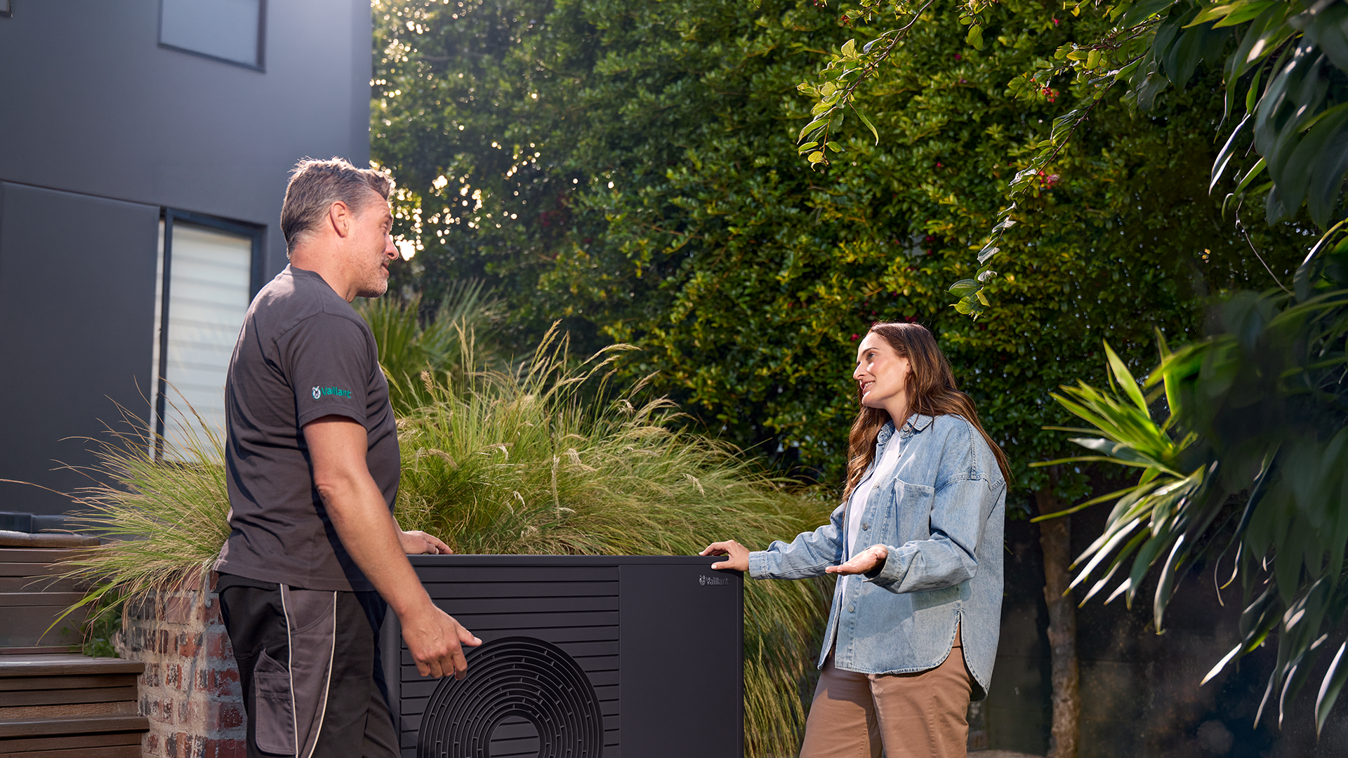 Fachinstallateur und Kundin vor Wärmepumpe im Garten