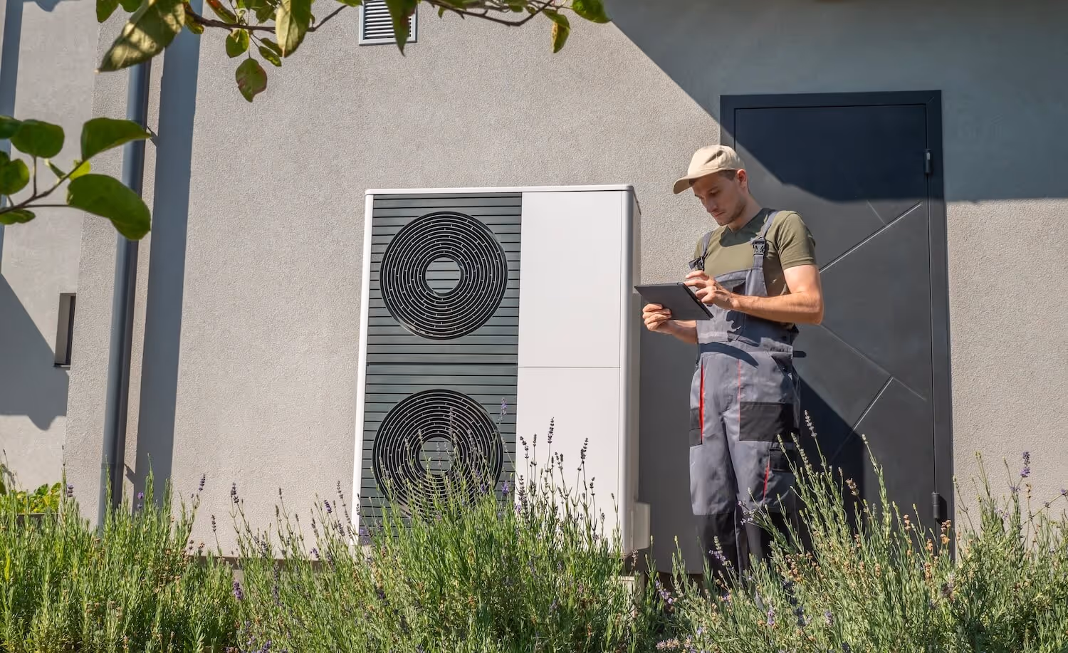 Handwerker mit Tablet in der Hand neben Wärmepumpe im Garten