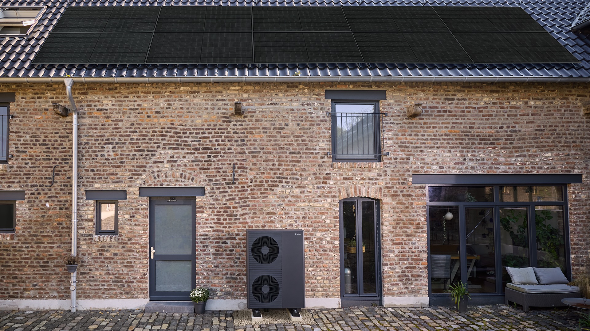 Altbau mit PV-Anlage auf dem Dach und Wärmepumpe vor dem Haus