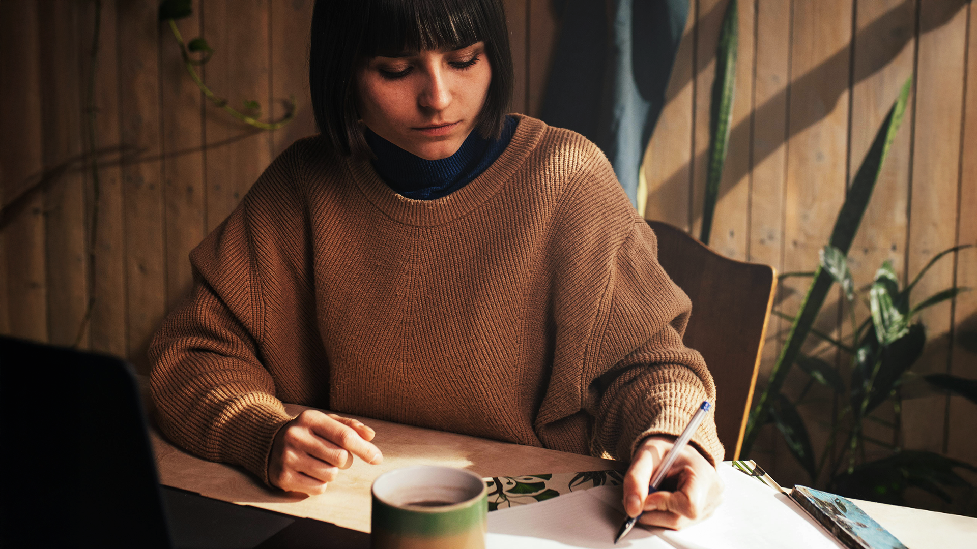 Frau mit Stift und Notizheft vor einem Laptop