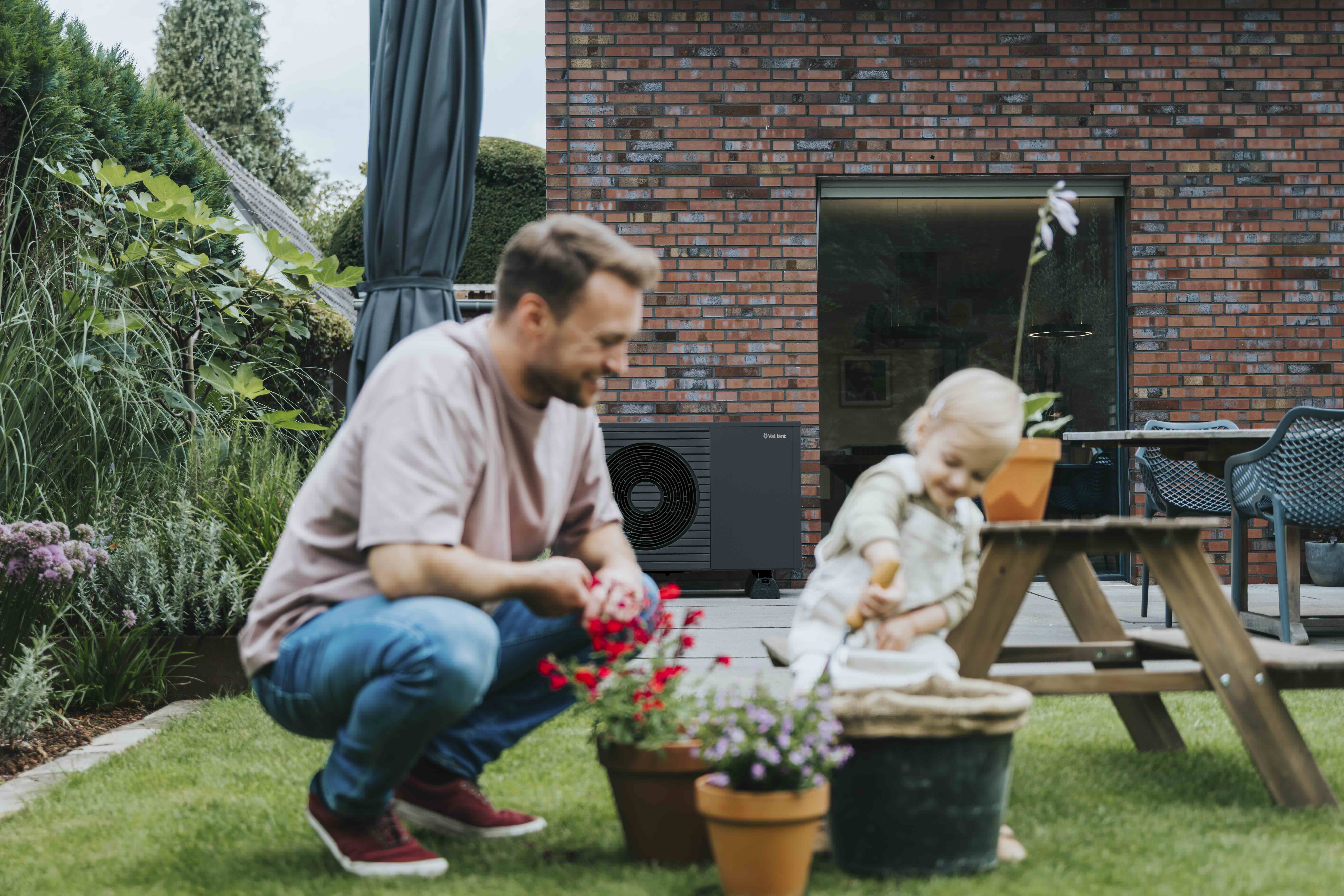 Vater spielt mit Kind im Garten, im Hintergrund Wärmepumpe auf der Terrasse