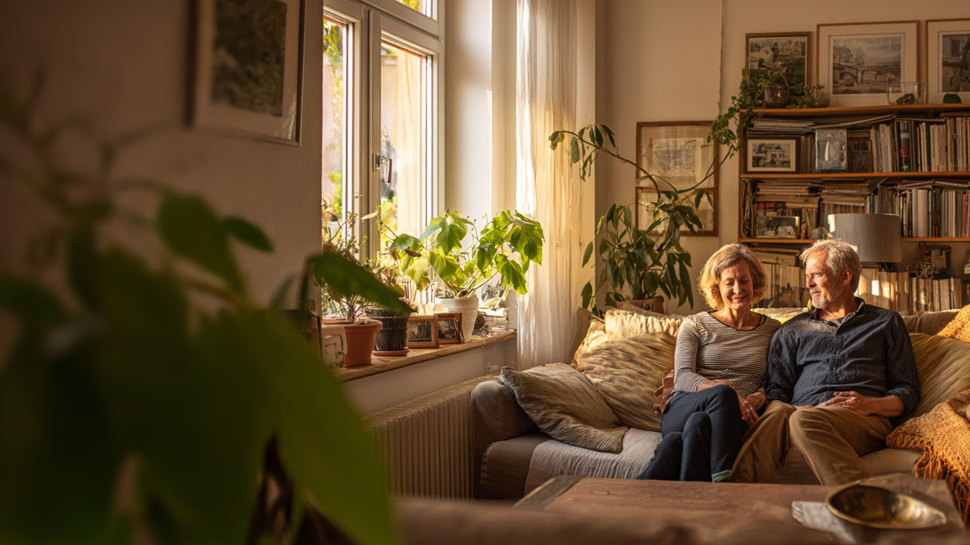 Paar sitzt gemeinsam auf dem Sofa, die Sonne scheint in das Wohnzimmer