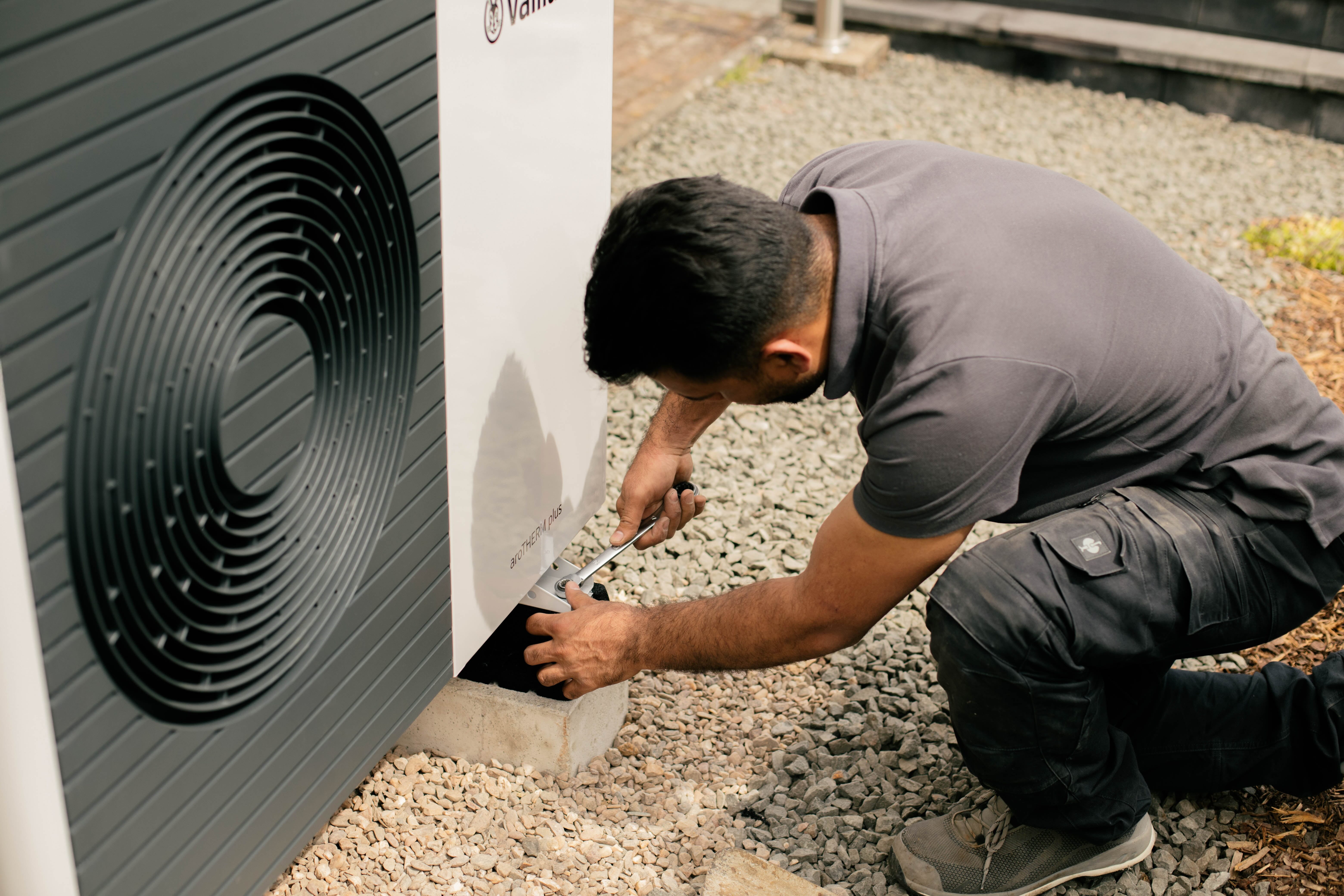 Installateur kniet mit Werkzeug vor einer Wärmepumpe