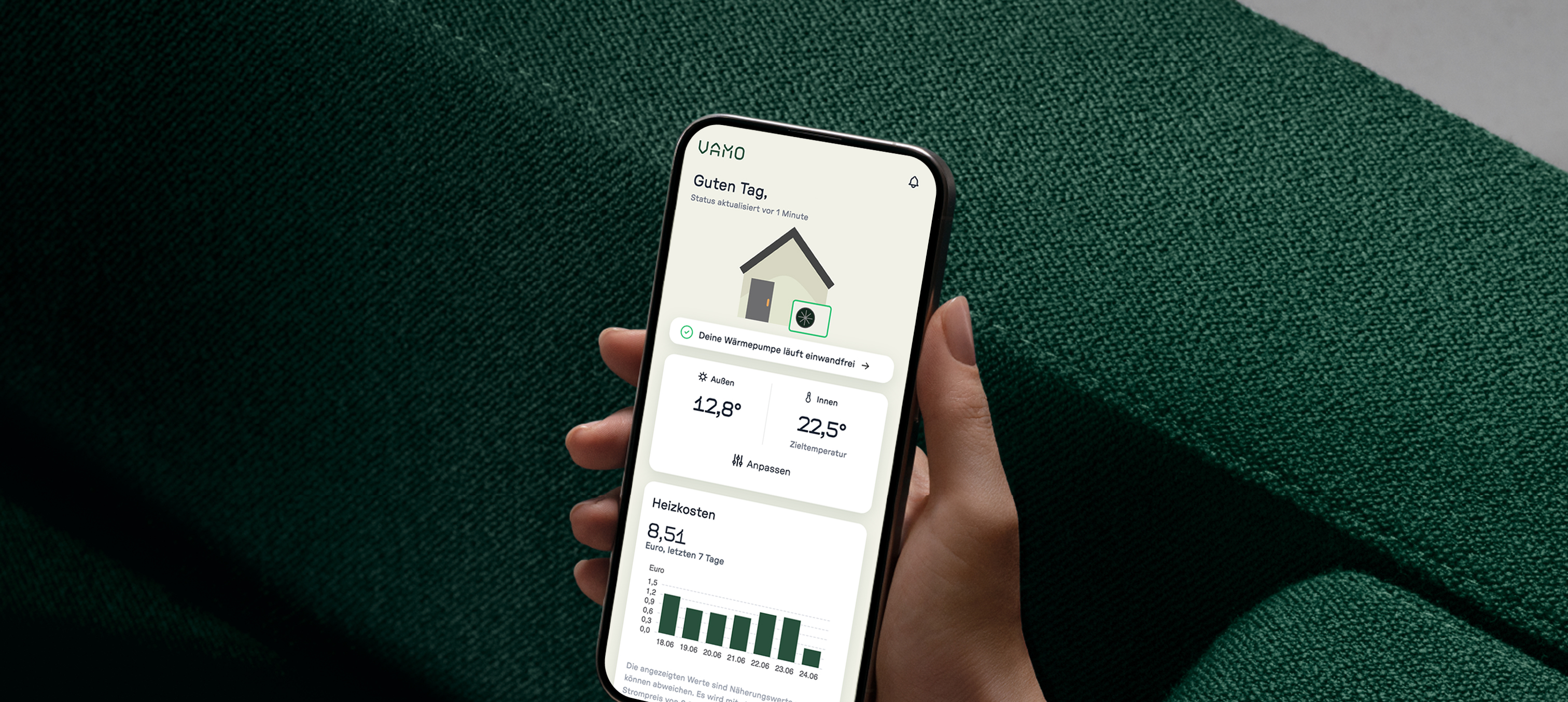 Handy in einer Hand vor grünem Sofa, die Vamo App geöffnet