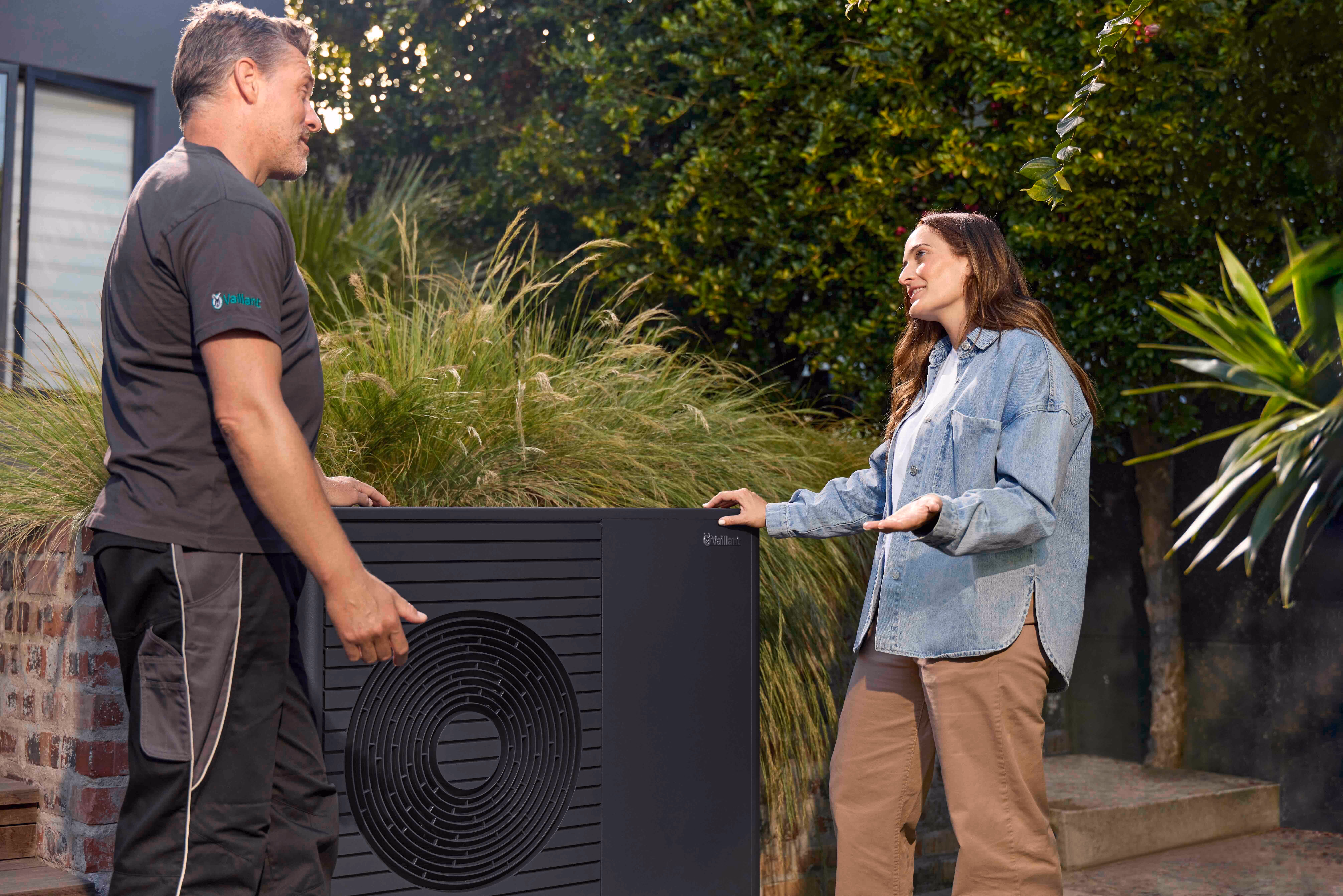 Installateur und Kundin vor der Wärmepumpe im Garten