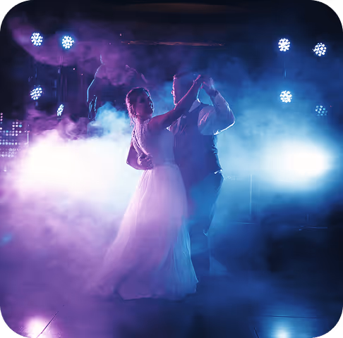 Bride and groom dancing together on a foggy, blue and purple lit dance floor.