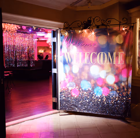 Open doorway leading to a colorful, glittery party room with a large 'Welcome' banner and shimmering decorations.