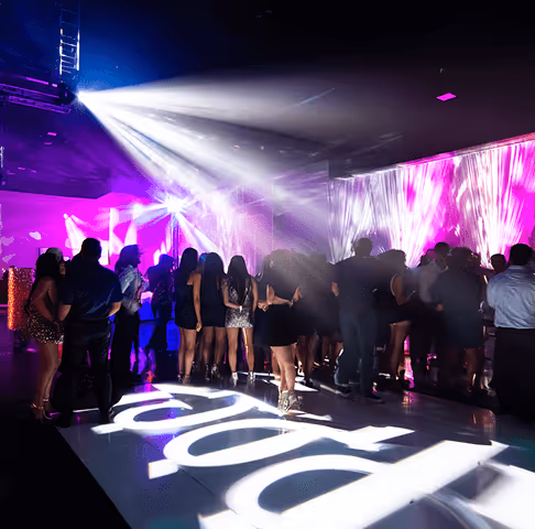 Crowd of people dancing under bright white and purple lights in a nightclub.