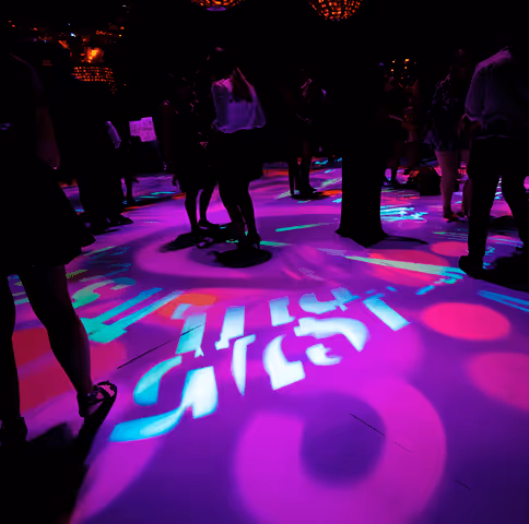 People standing and dancing on a floor with colorful pink and blue light projections.